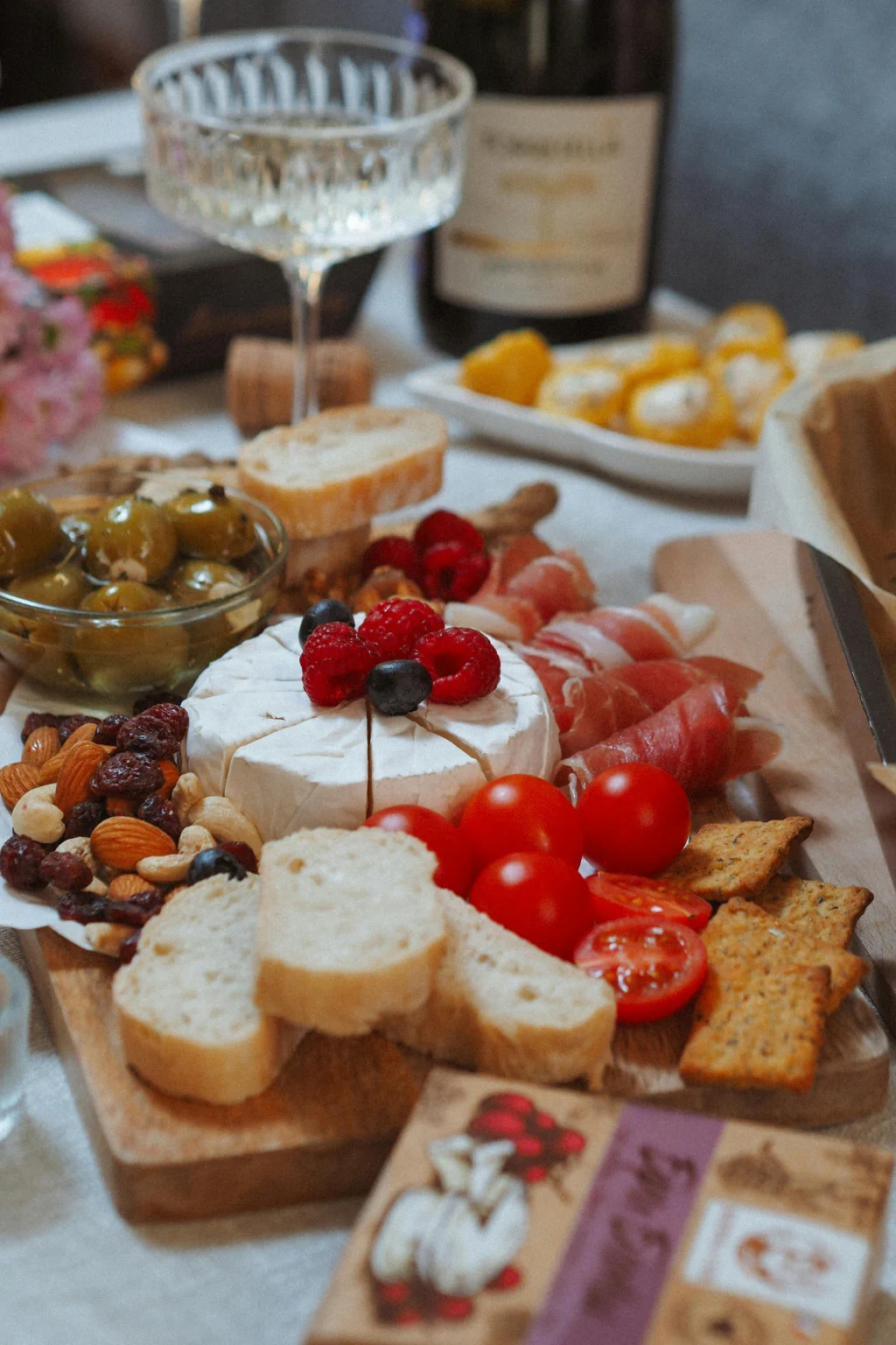 Styled charcuterie board with brie, berries, tomatoes, wine, and artisan crackers